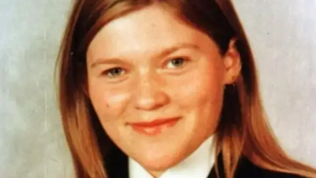 Lorraine Wilson has long blonde hair and is wearing a school uniform - it has a navy blazer, white shirt and a red tie.