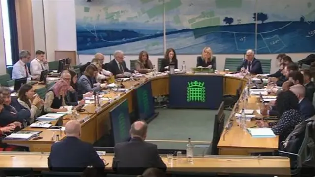 MPs sit around a semi circle table with the House of Commons branding