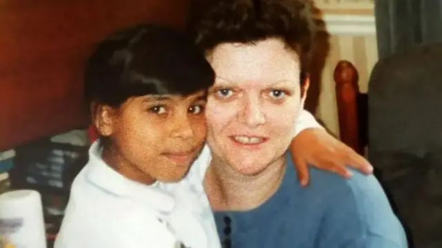 Philomena Skelton pictured with her daughter. Philomena has short brown hair and is wearing a blue top. Her daughter has black hair tied up in a ponytail and wearing a white jumper. She is hugging Philomena