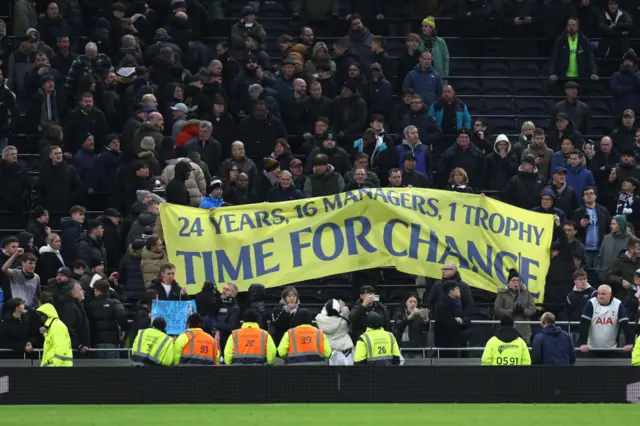 Tottenham fans hold a banner that says "24 years, 16 managers, 1 trophy, time for change".