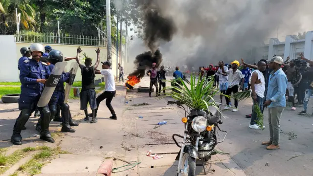 Protesters confront security officers outside the French embassy in Kinshasa on Tuesday morning. Behind them in the streets is a burning tyre.