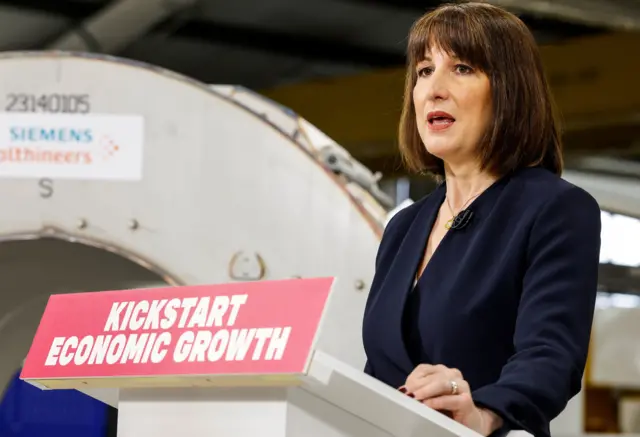 Rachel Reeves in a navy blazer stood behind a podium that says kickstart economic growth