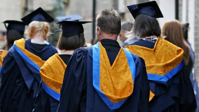 Students wear graduating caps and gowns, with the hoods coloured yellow and blue