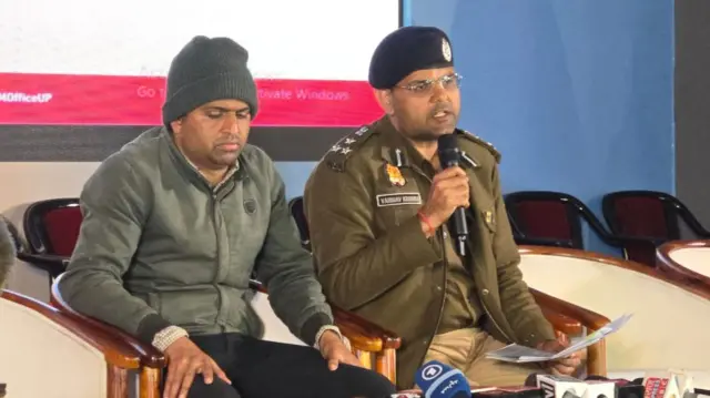 Vijay Kiran Anand, the official in charge of the Mela, gives a press conference. He holds a microphone and is dressed in military garb.