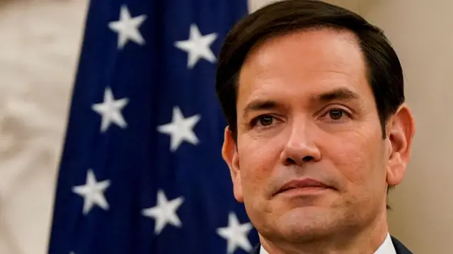 Secretary of state Marco Rubio stands in front of an American flag