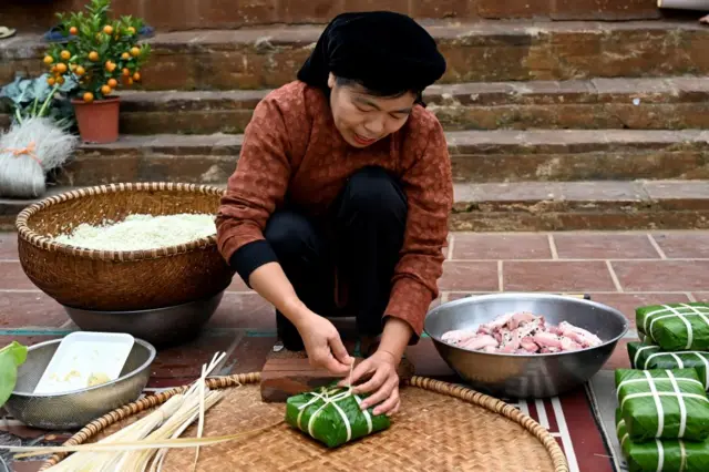 A woman wrapping banh chung rice cake, a traditional Vietnamese lunar new year or Tet festival delicacy, in the yard of her house