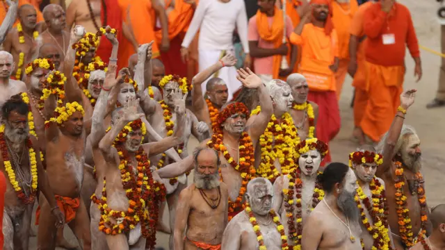 A group of men with ash smeared on them walk with flower garlands around their heads and neck