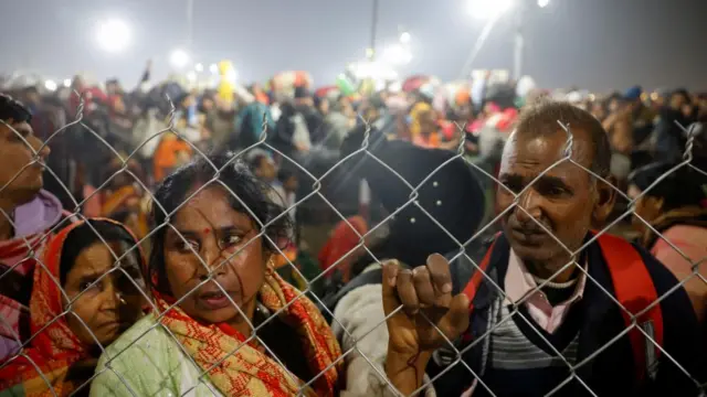 Hindu devotees are stopped by policemen after the crush - a man and a woman are standing behind a metal fence