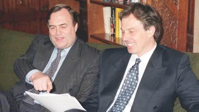 Prescott and Blair smile as they look at a piece of paper on a sofa