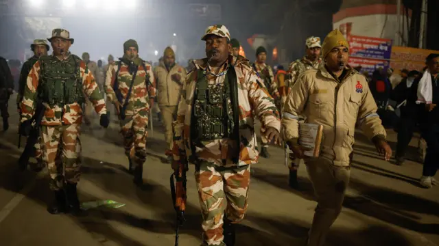 Men in brown camouflage uniforms walk in a line down a Prayagraj street at night