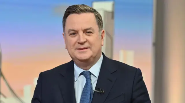 Shadow chancellor Mel Stride in blue suit and tie looking at the camera, smiling