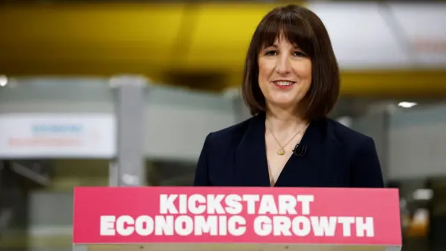 Rachel Reeves smiles while giving a major speech on economic growth this morning. She is standing at podium with a red sign that reads "kickstart economic growth".