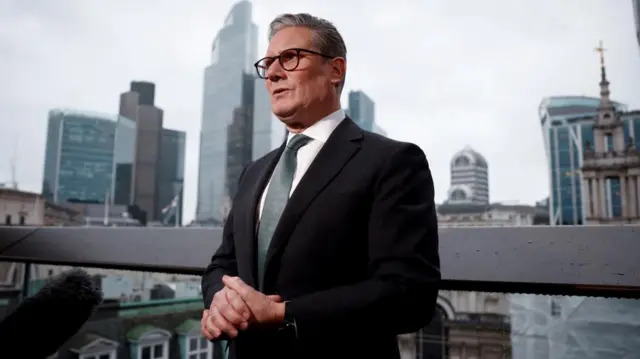 Keir Starmer in a suit stood on balcony overlooking London skyline