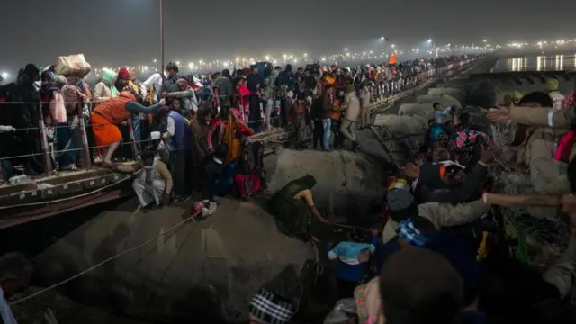 Massive crowds of pilgrims gather on a pontoon bridge with some individuals struggling to stand and others climbing over the fence.