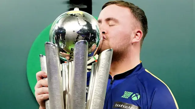 Luke Littler kisses the World Championship trophy