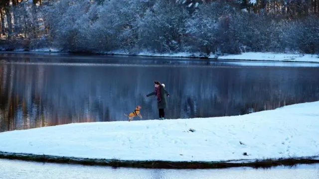 A person walks their dog through snow in the Pentland Hills, Balerno, Edinburgh