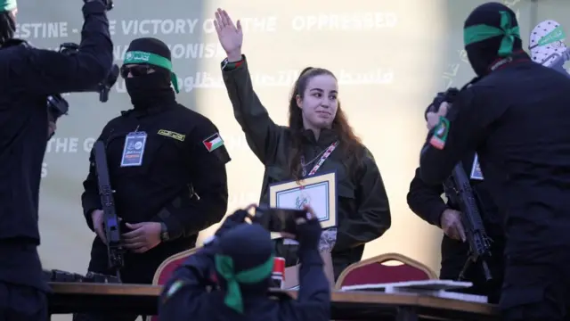 Woman with right hand up surrounded by armed men.