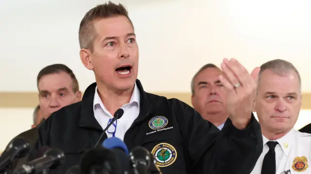 Secretary of U.S. Department of Transportation Sean Duffy addresses the media at a podium that has many microphones attached to it.