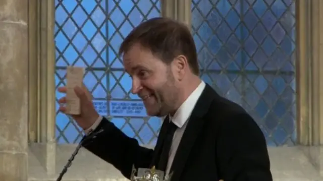 David Prescott holds up a copy of his father's speech in his right hand while smiling to funeral guests