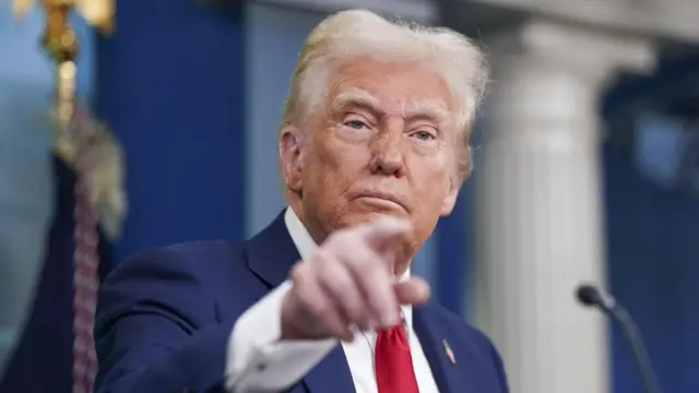 President Donald Trump points a finger and wears a red tie and blue suit