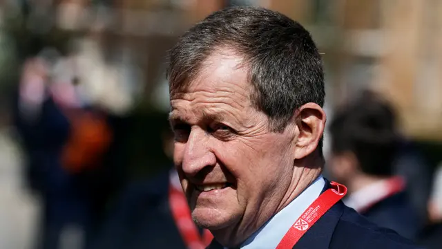 Alastair Campbell at an event in Northern Ireland in dark suit with a red lanyard around his neck