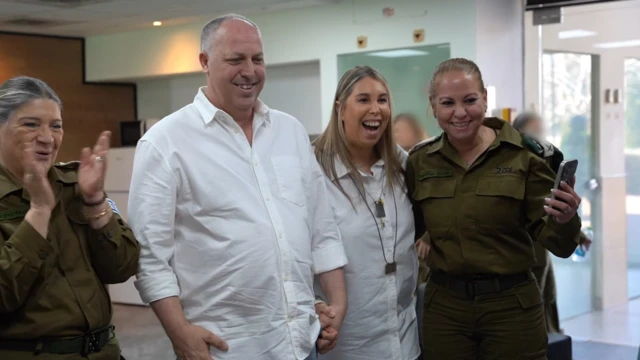 A man and a woman, wearing white shirts, stand between two IDF soldiers in uniform, all smiling.