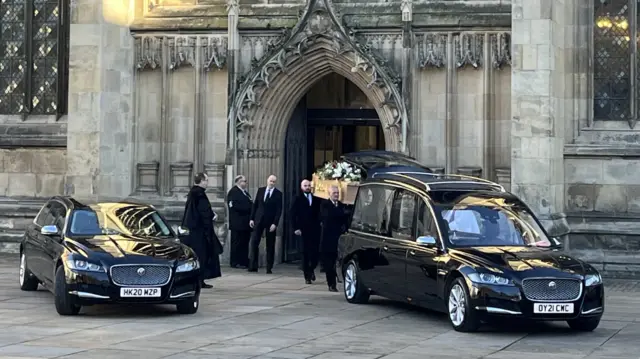 Pallbearers load Prescott's coffin into the back of a hearse outside the front doors of Hull Minster