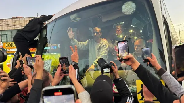 People surround and record a bus filled with passengers