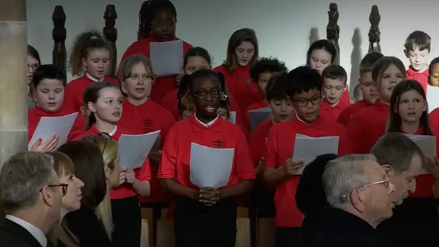 School choir in red shirts holding music sheet perform insider Hull Minster