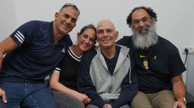 Family photo of Gadi Moses wearing a grey and black zip-up hoodie sat with his three children, all smiling