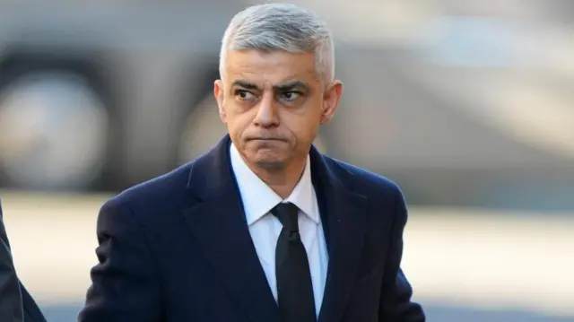 Khan, wearing a black suit, looks to the left