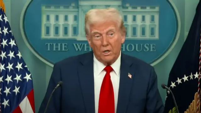 Mid shot of Donald Trump delivering speech in dark suit, red tie and white shirt, the White House logo behind him