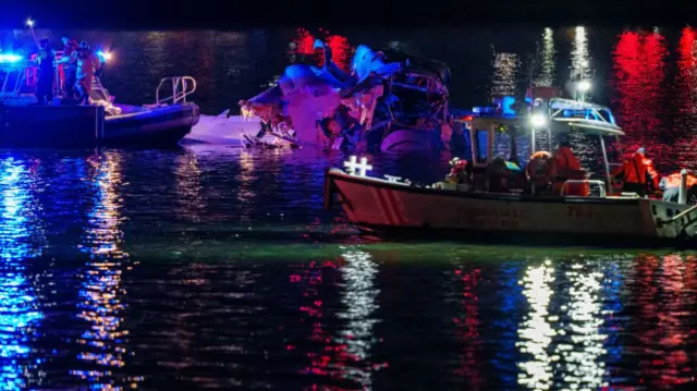 Emergency responders on the Potomac River in boats with partially submerged aircraft in river. Night scene with lights reflecting off water