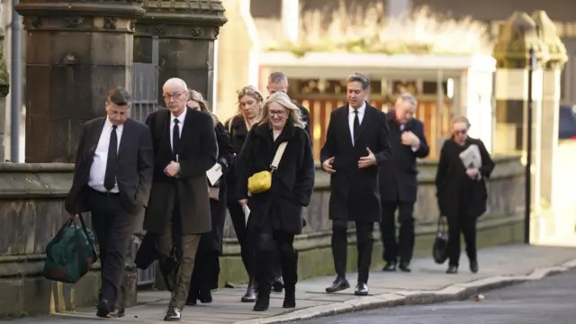 In a group of nine people wearing black walking along a footpath, Smith can be in front, with Miliband and Kyle chatting at the back