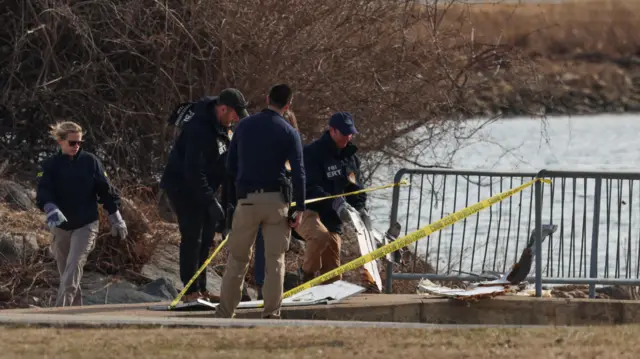 Law enforcement officials look at debris that has been brought up on the bank of the river. Yellow tape is around the debris.