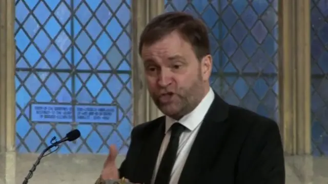 David Prescott in black suit, black tie and white shirt deliver speech in honour of his dad