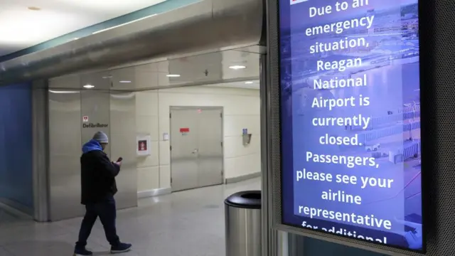 A man walks by a sign that says due to an emergency, the airport is closed