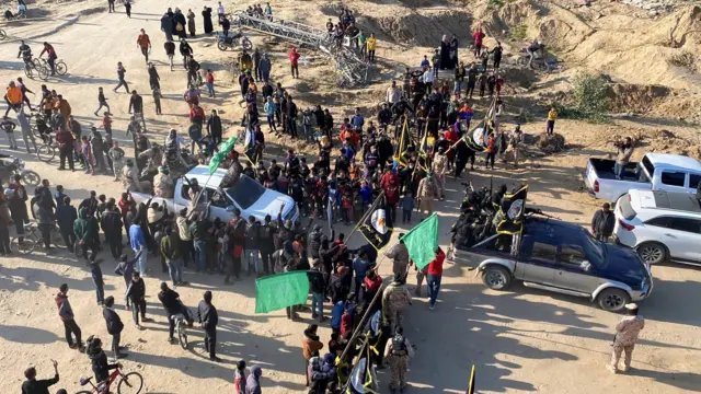 A large crowd gathers with cars and flags dotted around the scene.