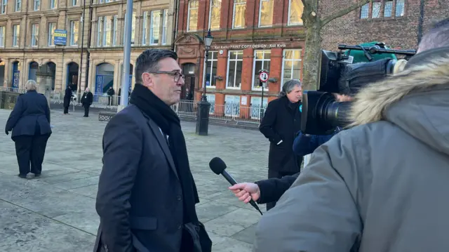 Andy Burnham speaks to a film crew outside the service