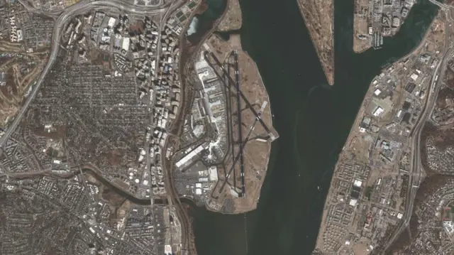 Aerial view of airport and river, with small white boat and debris visible in the water