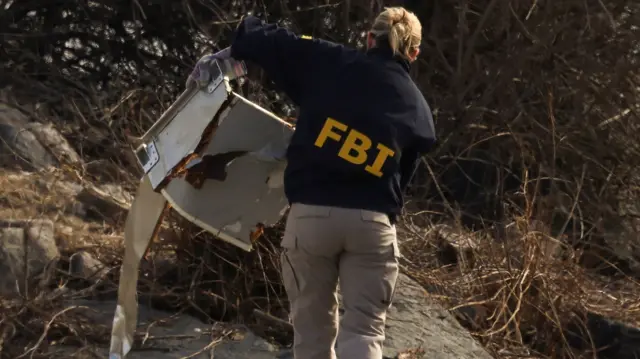 A woman with FBI written on her back in yellow letters holds up some debris