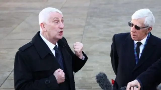 Lindsay Hoyle answers questions from journalists outside Hull Minster in black coat as Jack Straw, also in a black coat and sunglasses, stands to his left