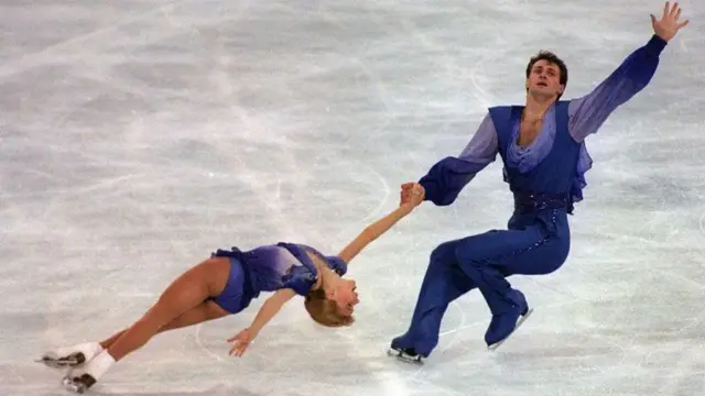 Evgenia Shishkova and Vadim Naumov in blue outfits skating on the ice. with Evgenia holding Vadim's hand and being spun around