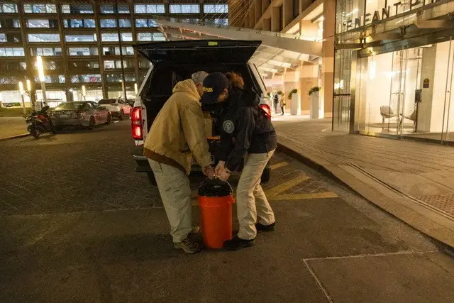 Two people behind the open boot of a car lifting an orange bucket together