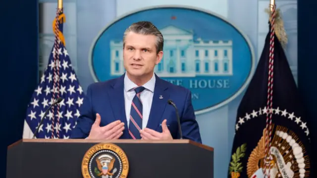 Headshot of Hesgeth speaking at a White House briefing with the US flag behind him