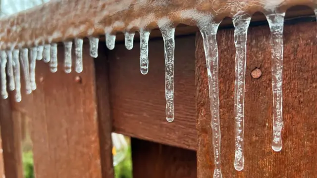 Brown wooden fence covered in icicles that have formed as long drops of water, frozen in place, above the ground