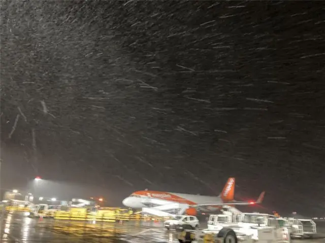 An Easyjet plane is on the runway, snow is falling above it.