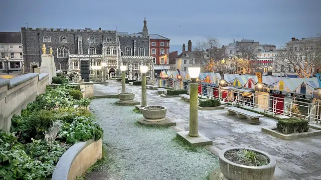 An overhead shot looking down on a public path with grass and frost on the left and market stalls on the right