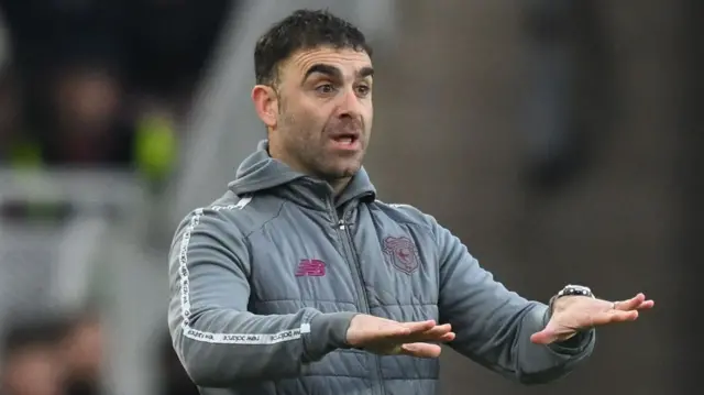 Cardiff manager Omer Riza lowers both hands, indicating his team needs to calm down