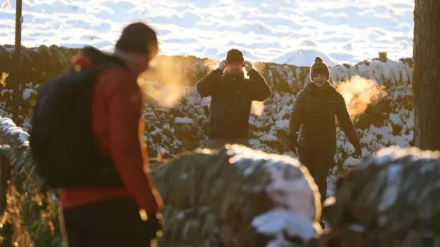 People walk in hiking gear on hill with rocks covered in snow